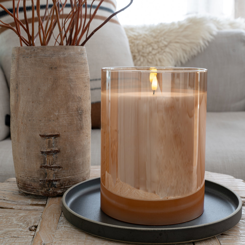 Amber flameless LED candle on a vintage table, placed on a black tray next to an antique wooden vase with reeds, creating a cozy and ambient lighting atmosphere.